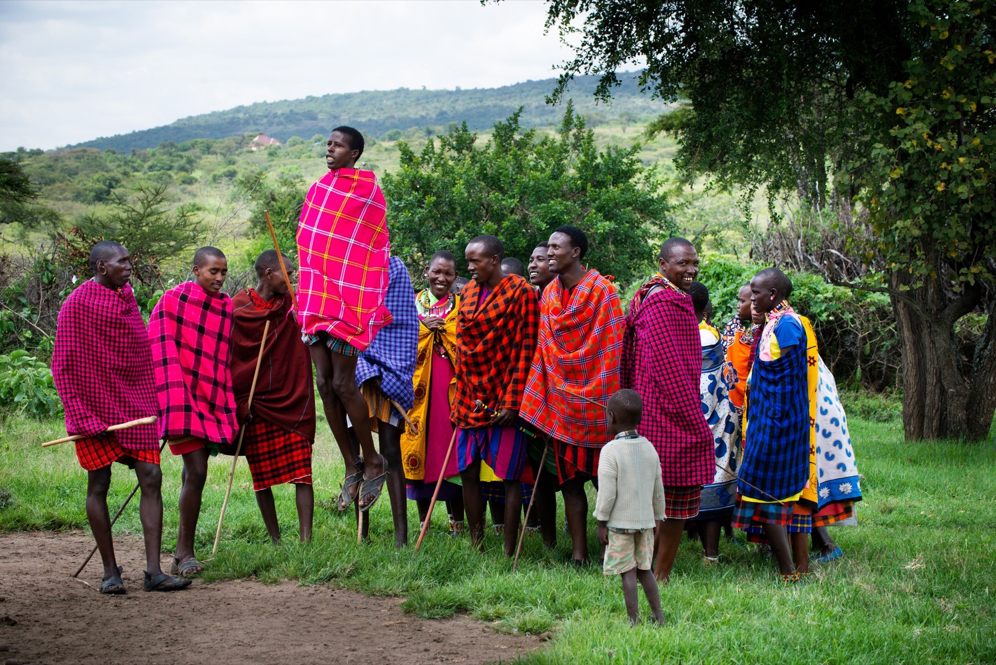 Maasai community members in colorful shukas gathered under a tree during a community visit