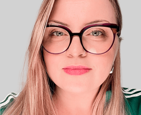 Casual studio portrait of a bearded man with curly hair in a white shirt, arms crossed, on a light gray background.