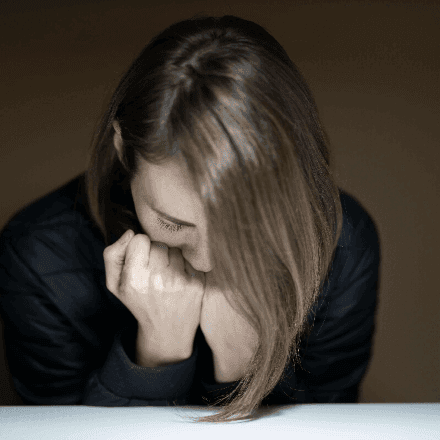 Woman with head down and hands clasped, showing emotional struggle and the relief accessible through HeadHealth expert counselling