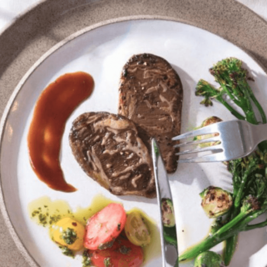 A delicious meal on a plate with a grilled steak, broccoli, and tomatoes.
