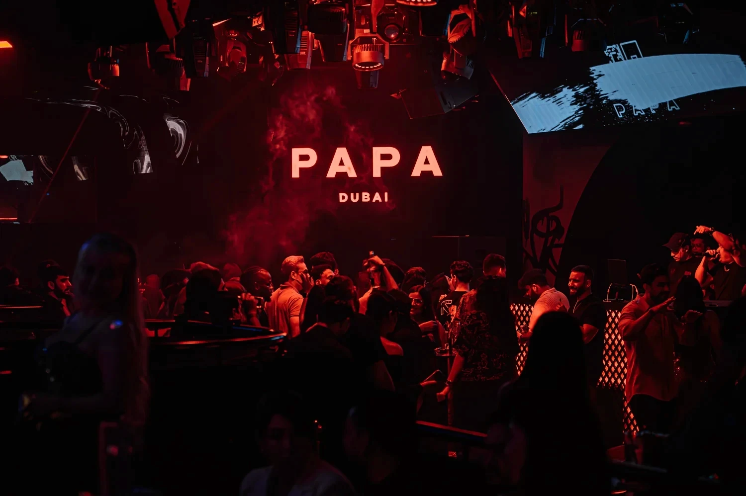 Glowing PAPA Dubai sign above a busy dance floor in red light and haze