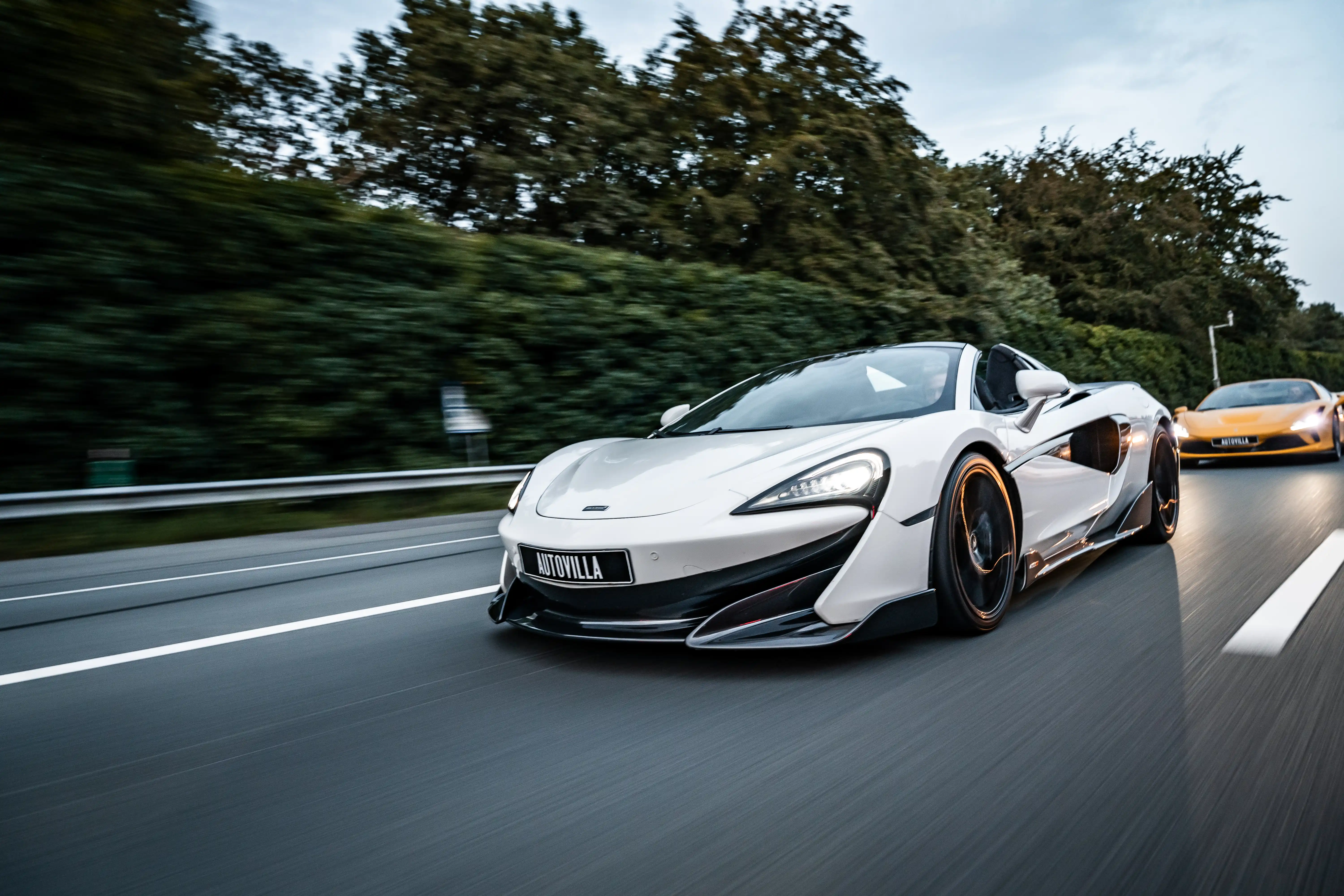 Frontside view of an Mclaren driving very fast on the highway with a Ferrari behind it