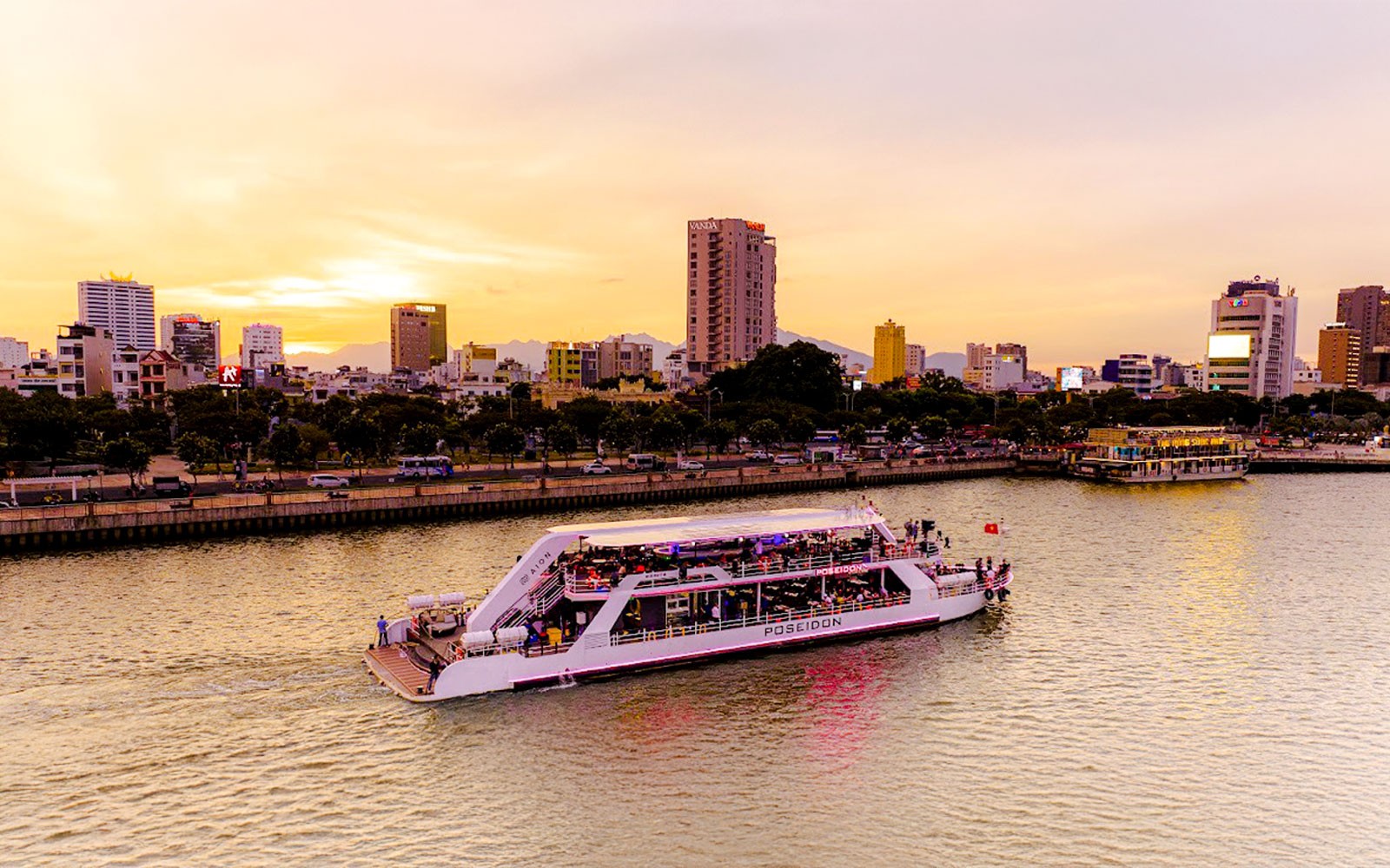 Da Nang Poseidon cruise on the river at sunset with city skyline in the background.