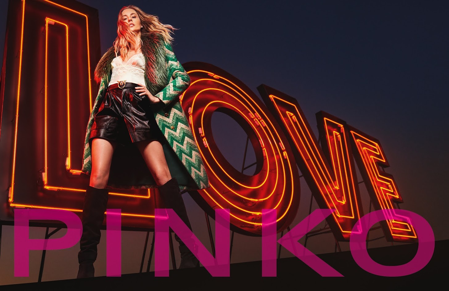 PINKO campaign visual featuring model in chevron coat against dramatic LOVE neon sign installation demonstrating brand's bold aesthetic and emotional storytelling approach - pandemic-era crisis communication and creative adaptation strategy by Alessandro Brancati Marketing & Growth Studio