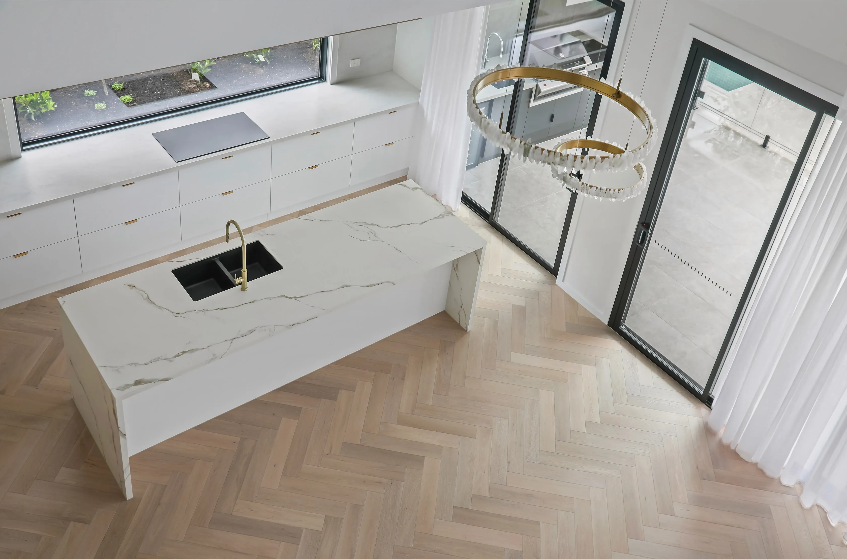 Overhead view of the Mount Waverley Residence kitchen island in marble-look stone with brass tap and crystal ring pendant lights