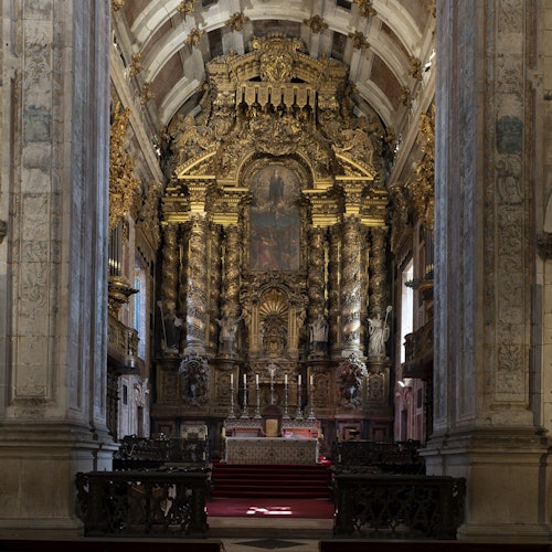 Elaborately decorated church altar with intricate carvings, gold accents, and a painting. Stone columns and pews are visible.