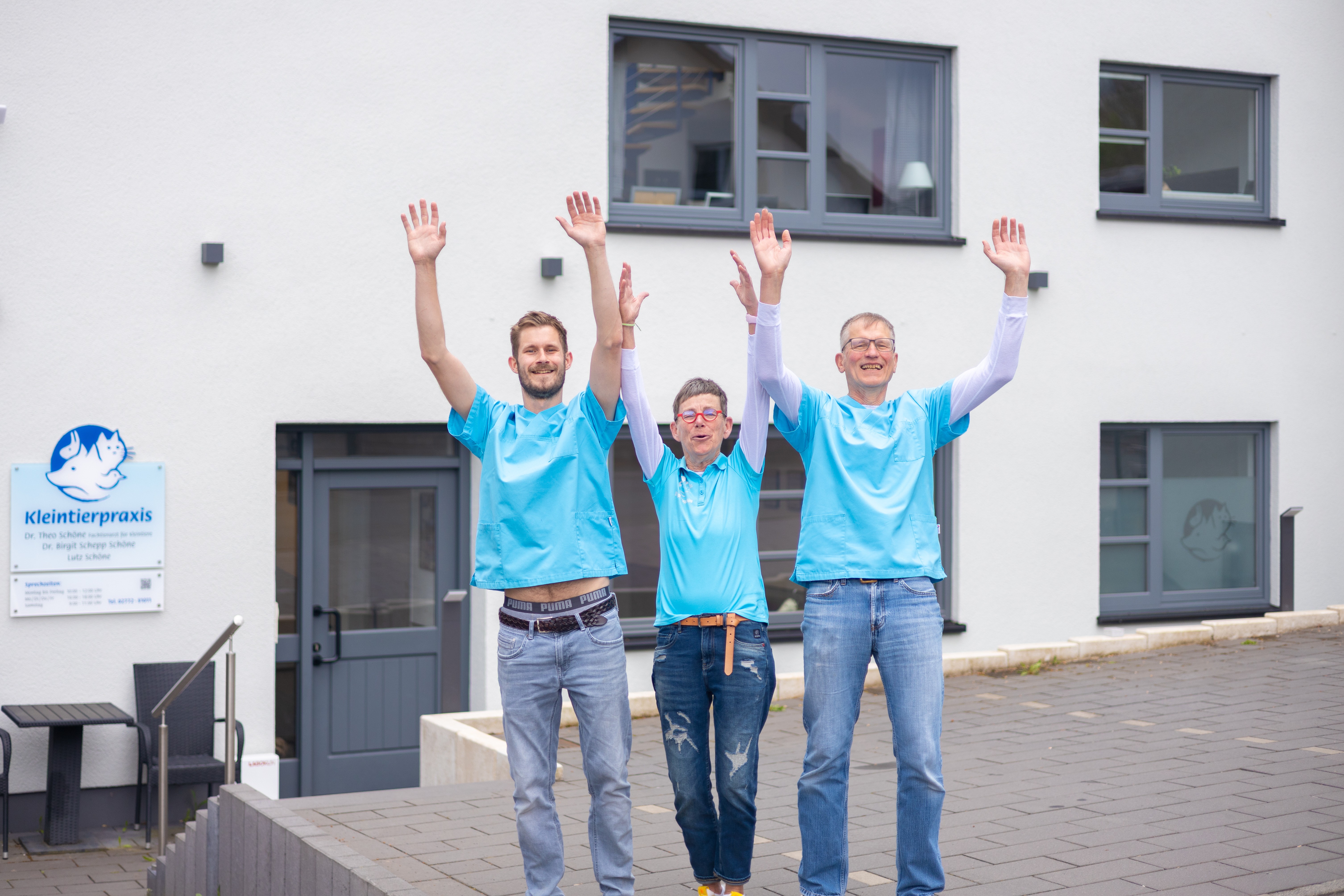 Drei lachende Tierarzt Angestellte,  Tierarztpraxis im Hintergrund,  blaue Kleidung,  Hände hochgestreckt