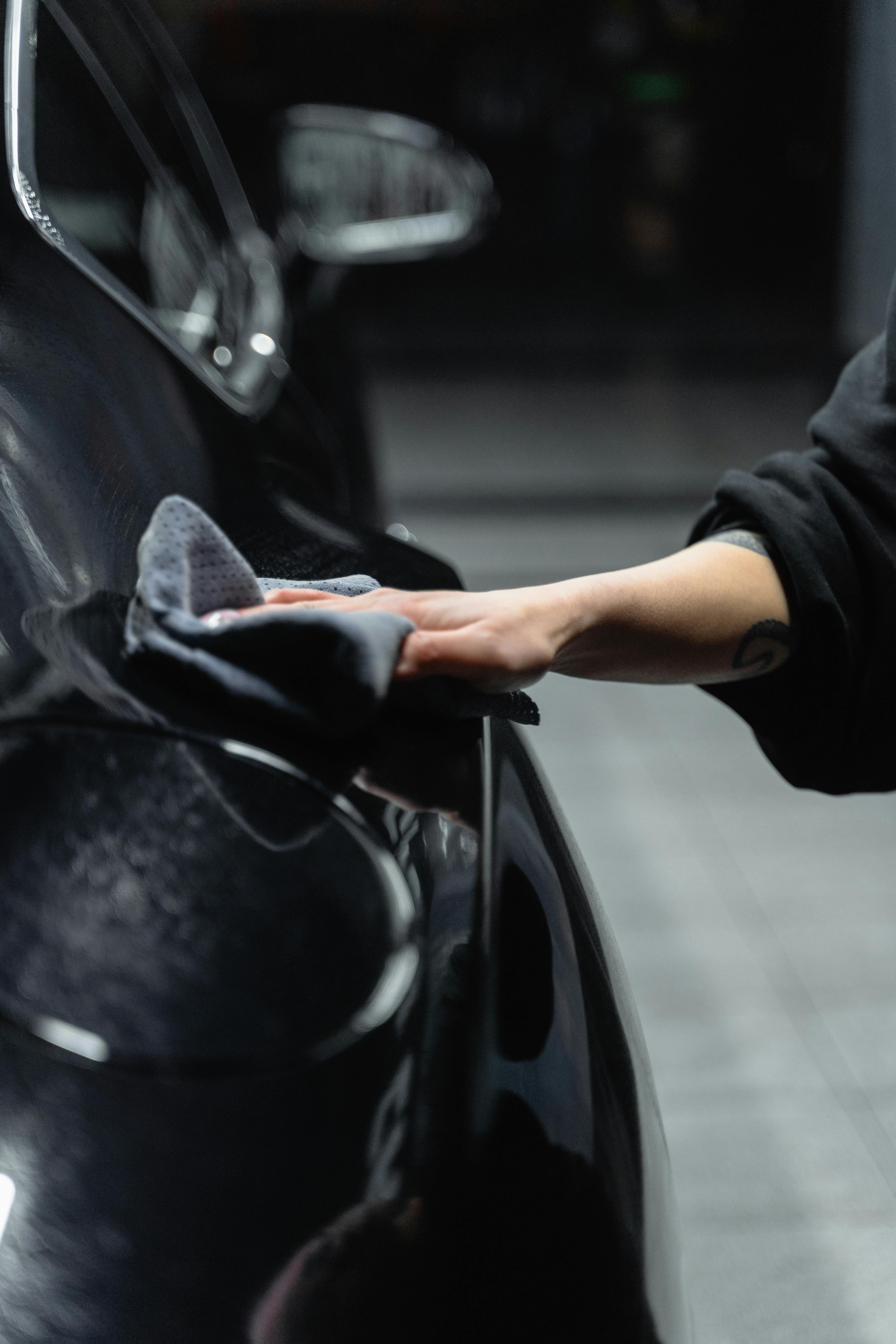 Person polishing a car and adding the finishing touches to a glossy surface, symbolizing attention to detail and perfection.