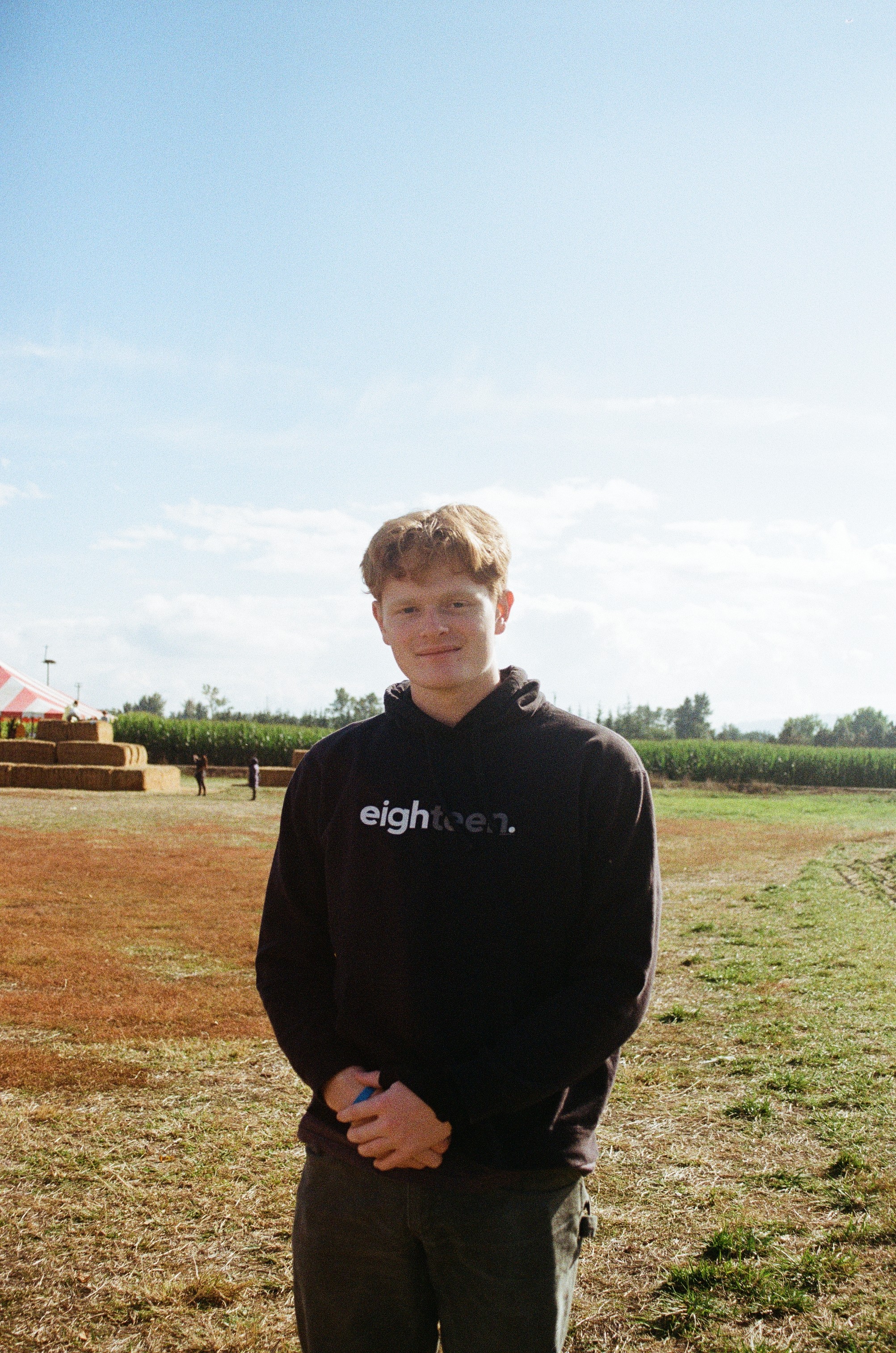Person wearing a blue puffer jacket and red backpack standing in front of a light blue building on a city street.