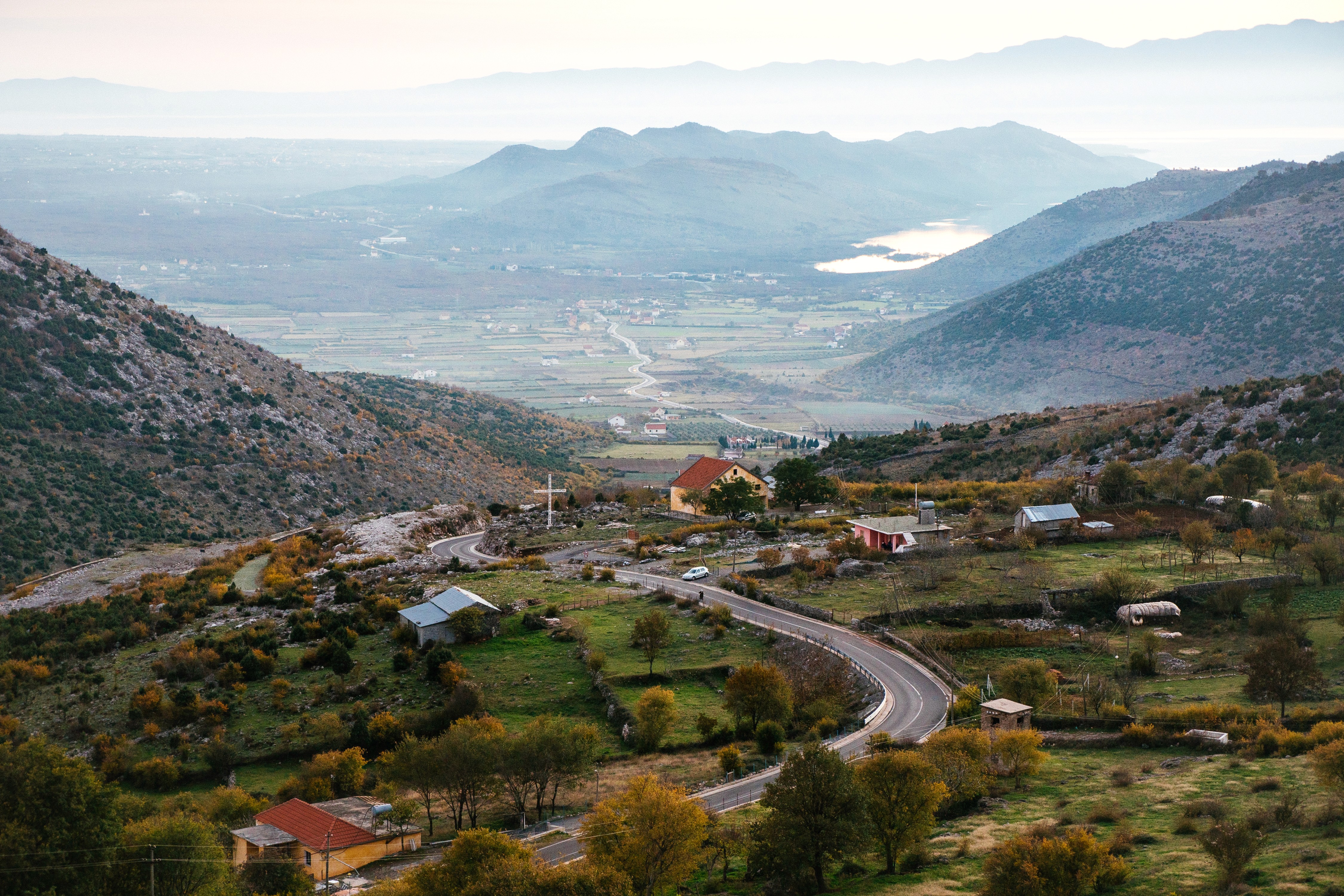 A person in white clothing walking through golden foliage, seen through large vertical glass panels that create fragmented reflections.
