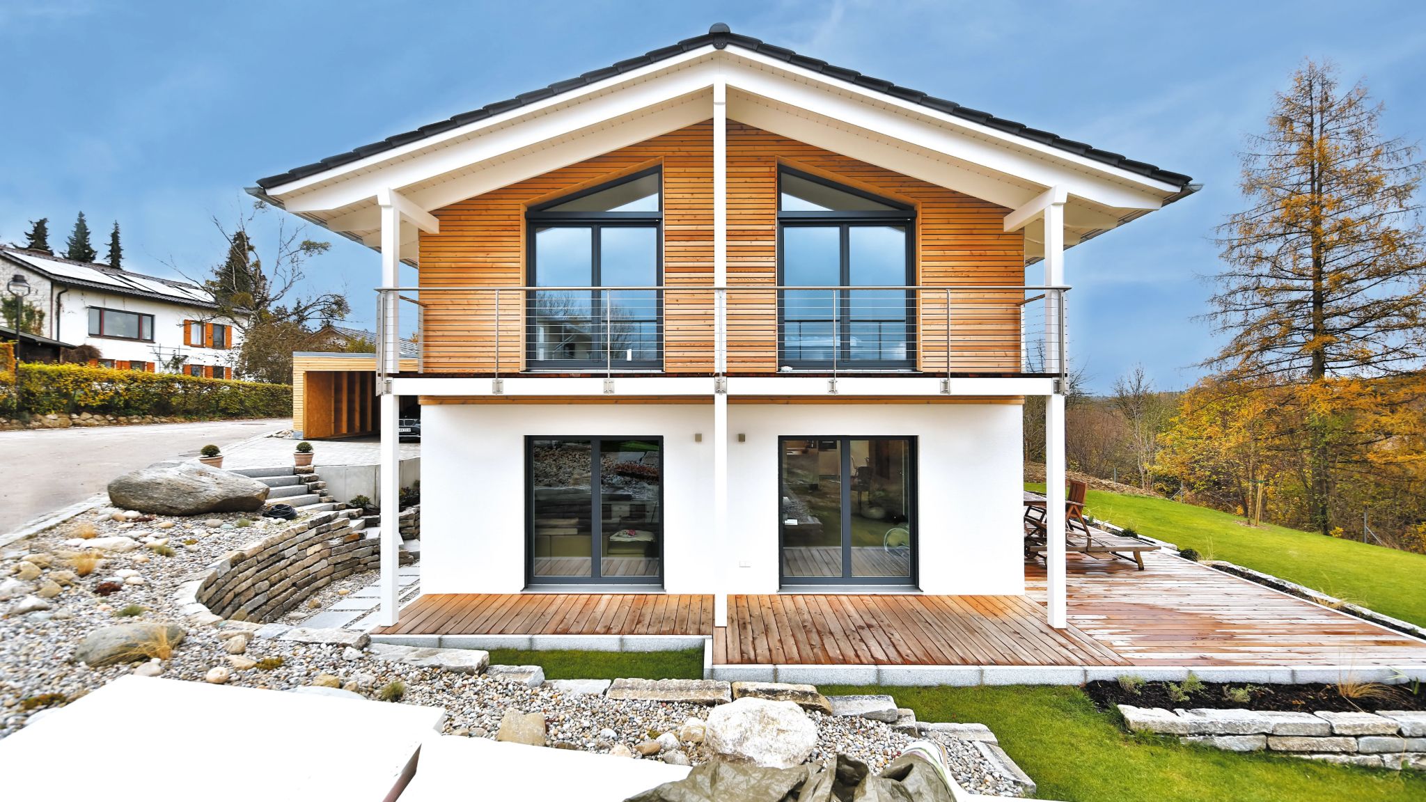 Modernes Einfamilienhaus mit Holzverkleidung und großzügigem Balkon, umgeben von Natur und einem angelegten Garten.