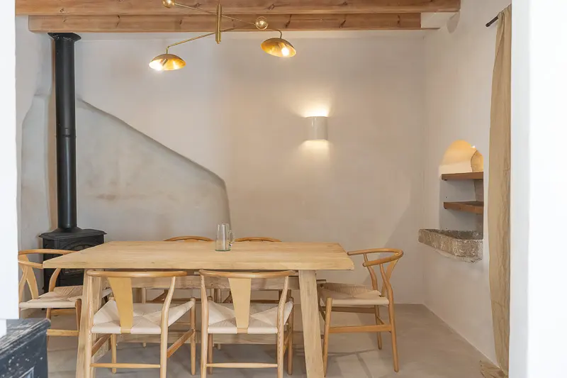 comedor con mesa de madera clara en el centro y chimenea pequeña negra al fondo