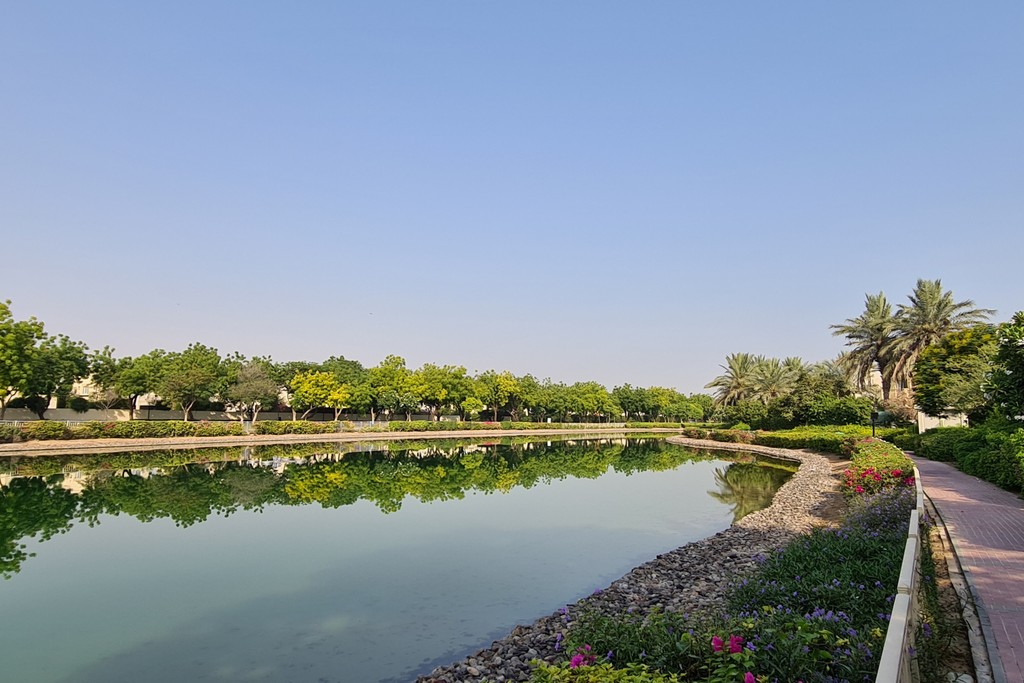A serene canal flows through a park adorned with vibrant trees and blooming flowers, capturing the essence of spring.