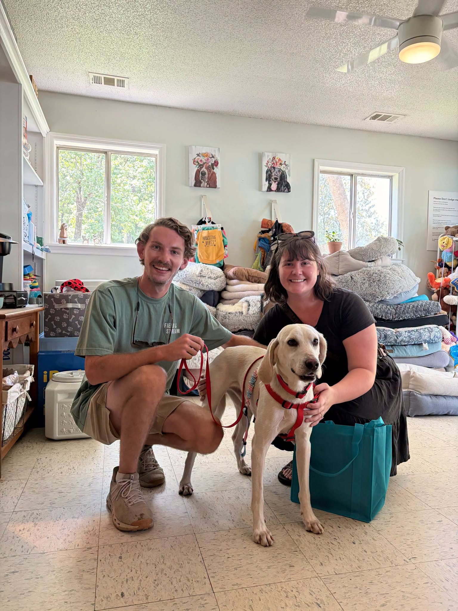Couple posing with their newly adopted cream-colored dog wearing a red harness inside the Raskel's Rescue adoption center.