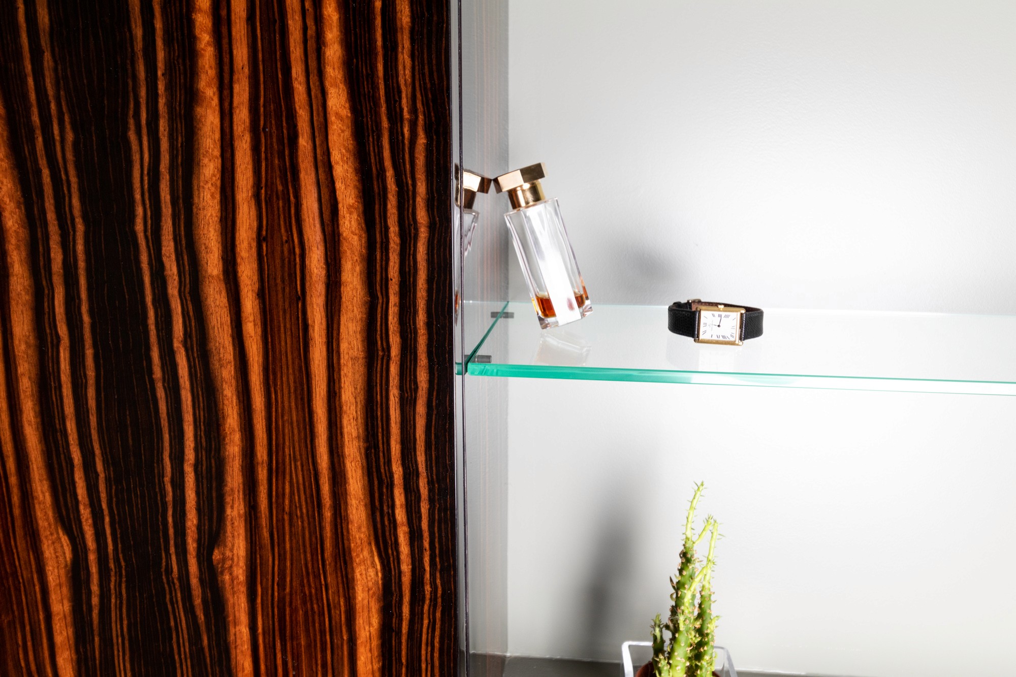 Photo d'une armoire de salle de bain avec une étagère en verre contenant une boutelle de parfum et une ancienne montre vontage