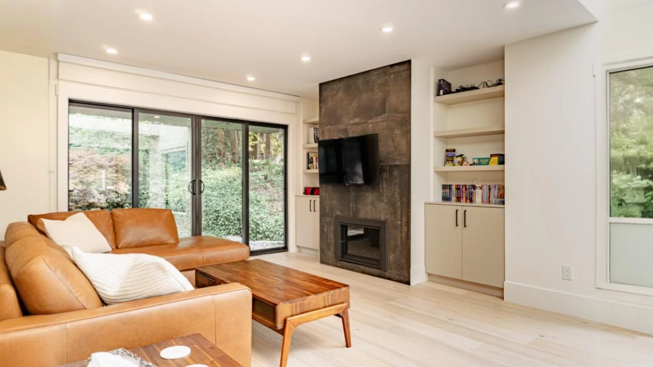 Family room featuring tan leather sofa, custom fireplace with built-in shelving, and sliding glass doors to backyard in Vancouver home