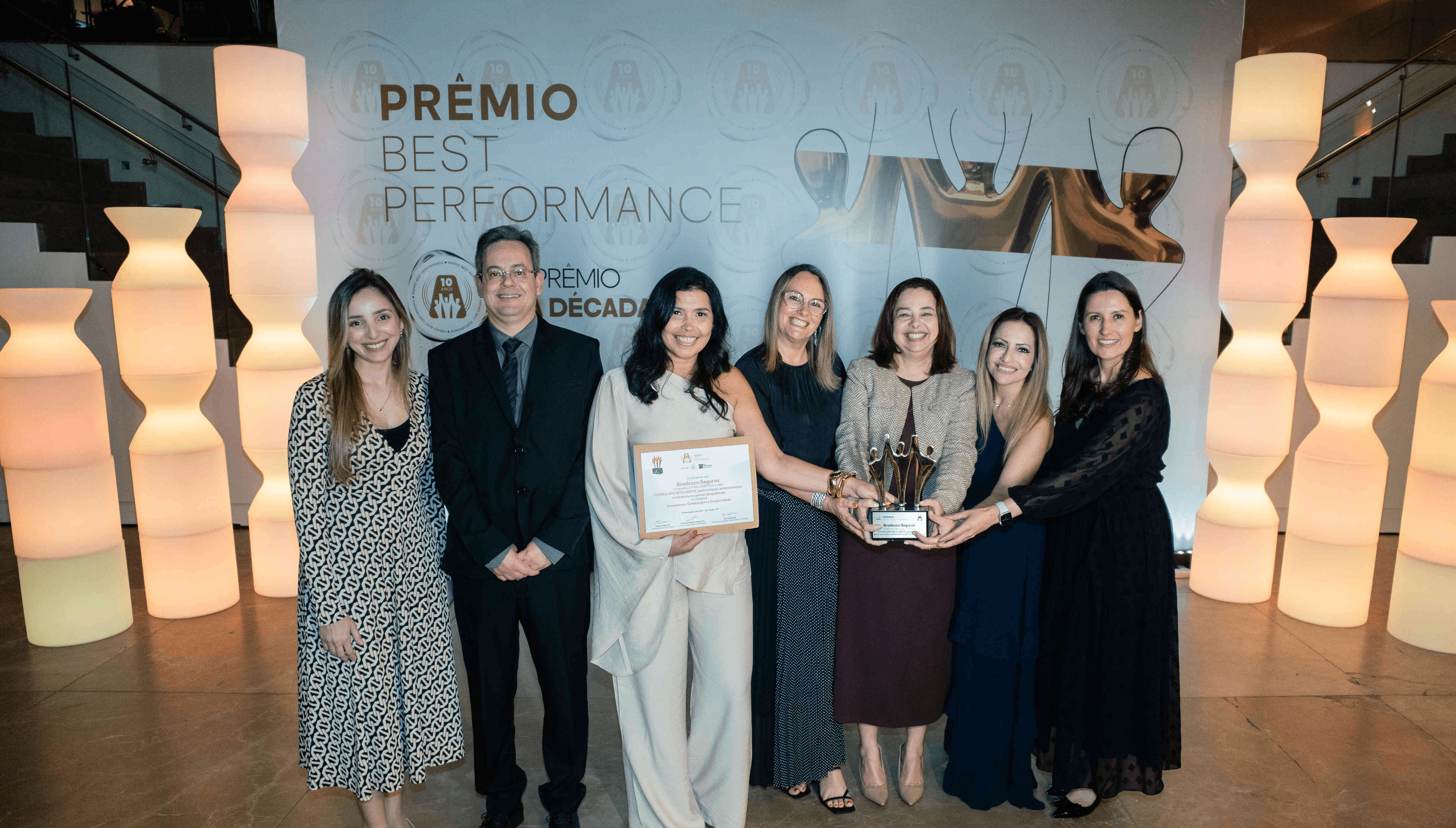 Executivos da Bradesco Seguros posando com troféu ouro e certificado no palco do Prêmio Best Performance 2025