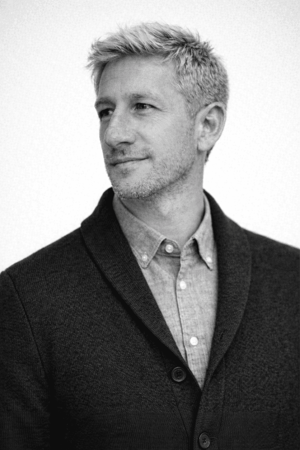 Portrait of a man with short dark hair and a trimmed beard, dressed in a dark shirt, on a simple background.