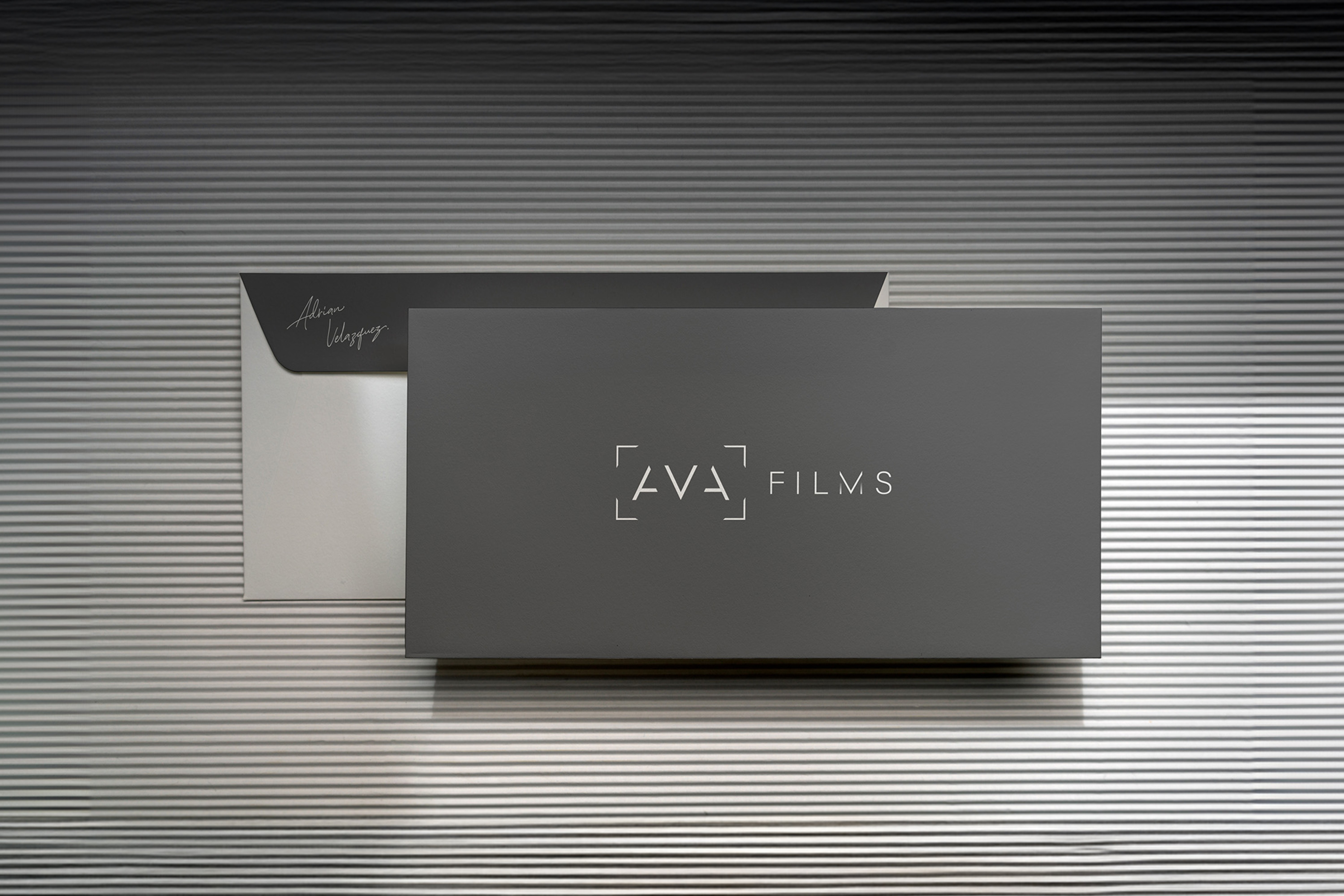  Luxurious black AVA Films business card with gold embossed logo, placed against a textured silver surface, reflecting a high-end videography brand identity.