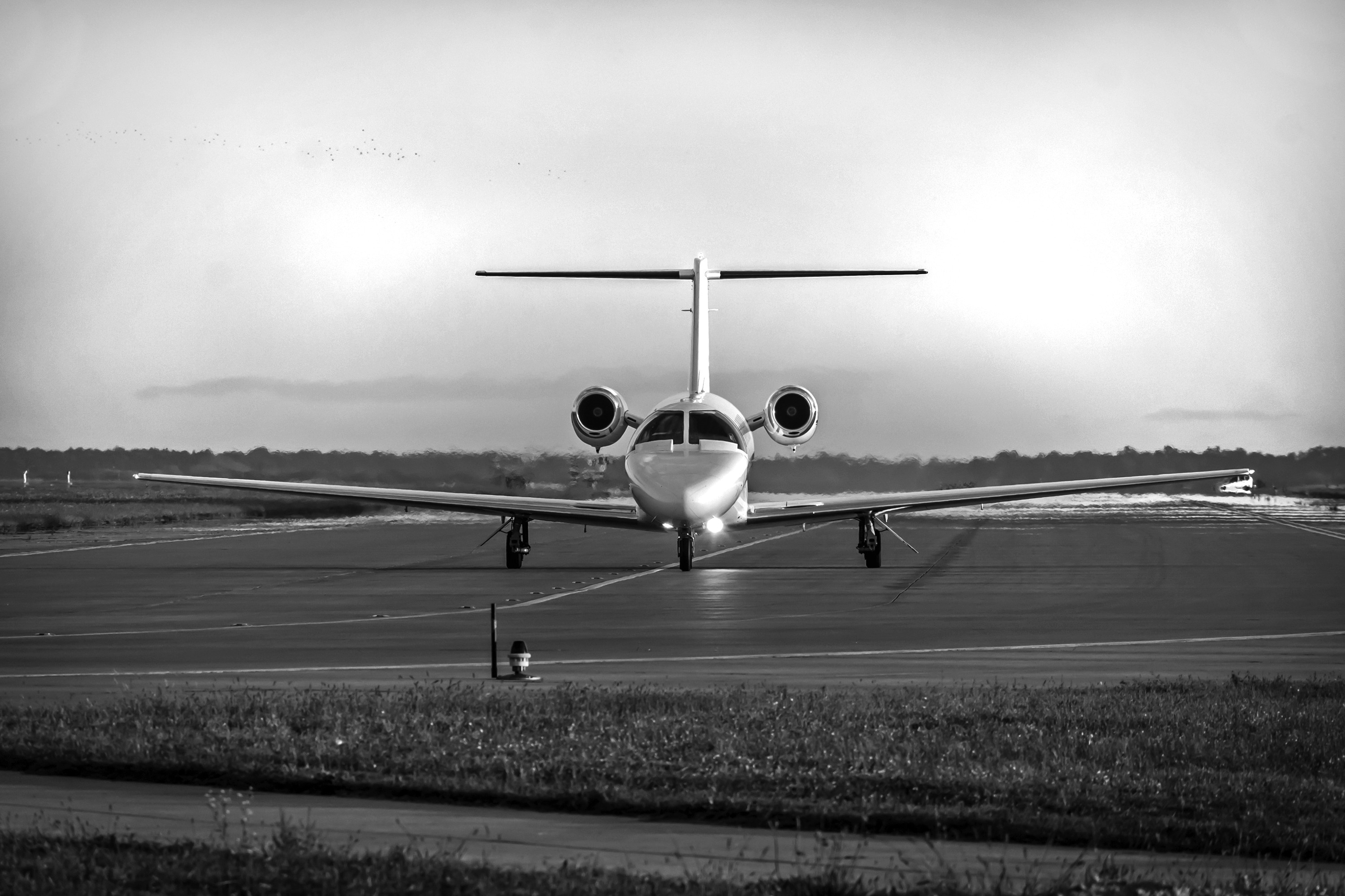 A black and white image of an airplane on a runway, with a cloudy sky in the background.