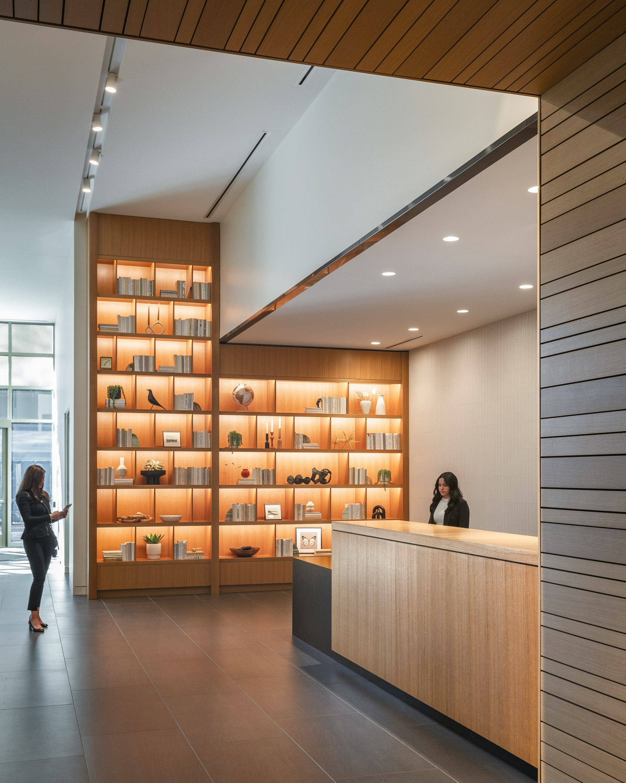 Reception desk area with a lit bookshelf and woman on phone