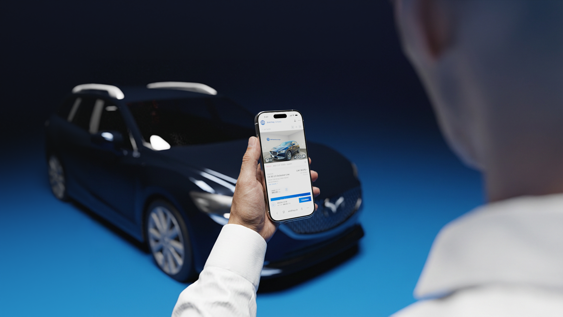Eine Person hält ein Handy in der Hand, auf dessen Display die Website von Emil Frey Switzerland zu sehen ist. Hinter dem Handy steht ein Automodell, das genau dem auf dem Handy abgebildeten Modell entspricht. 