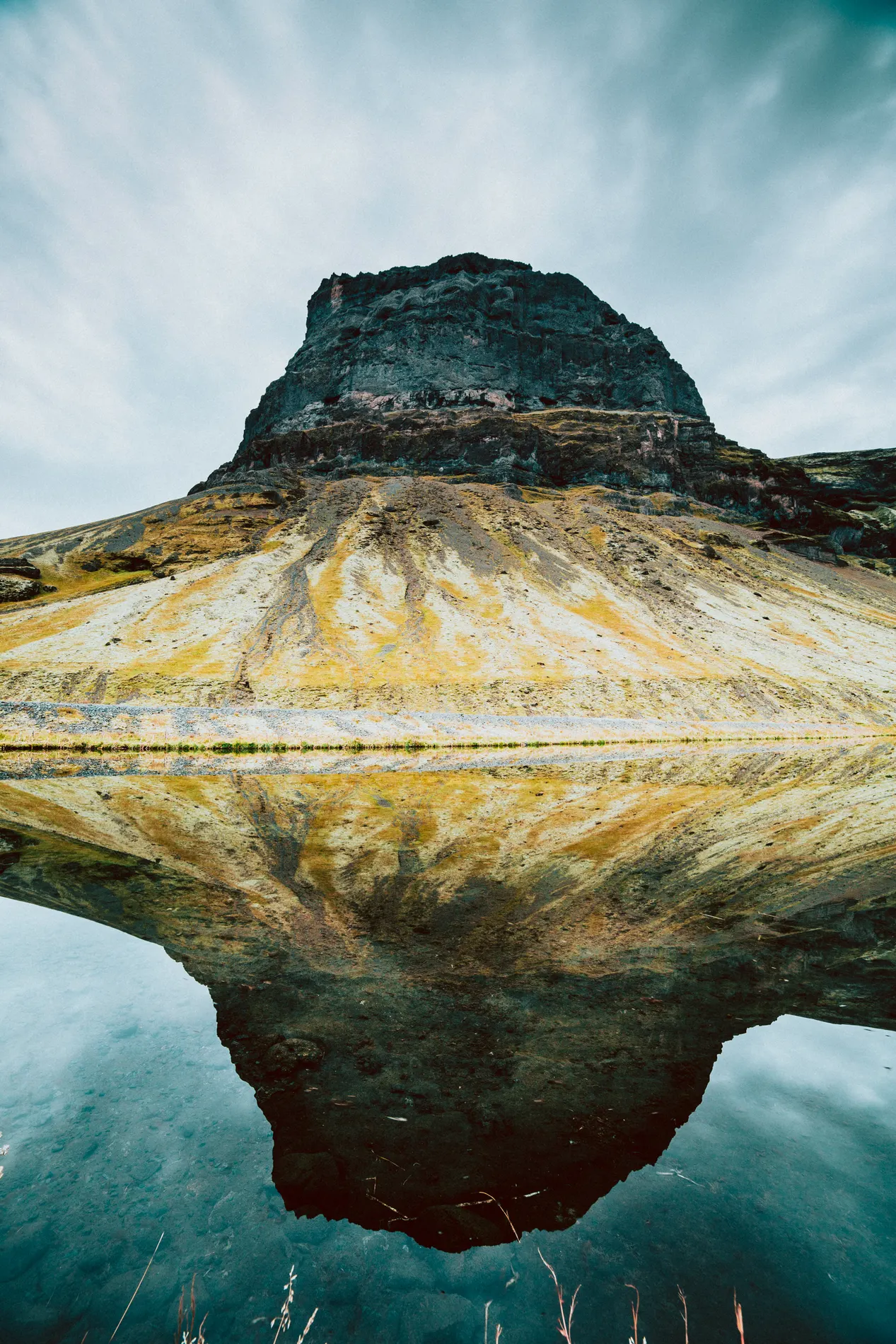 A steep dark peak mirrored in still water below