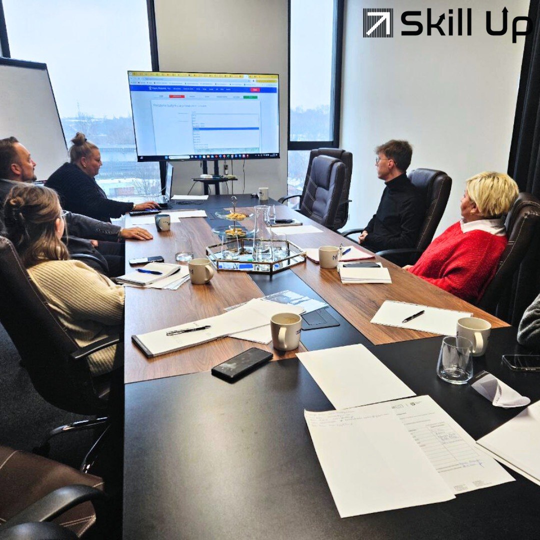 Flaga Unii Europejskiej powiewająca na wietrze przed nowoczesnym, przeszklonym budynkiem biurowym.