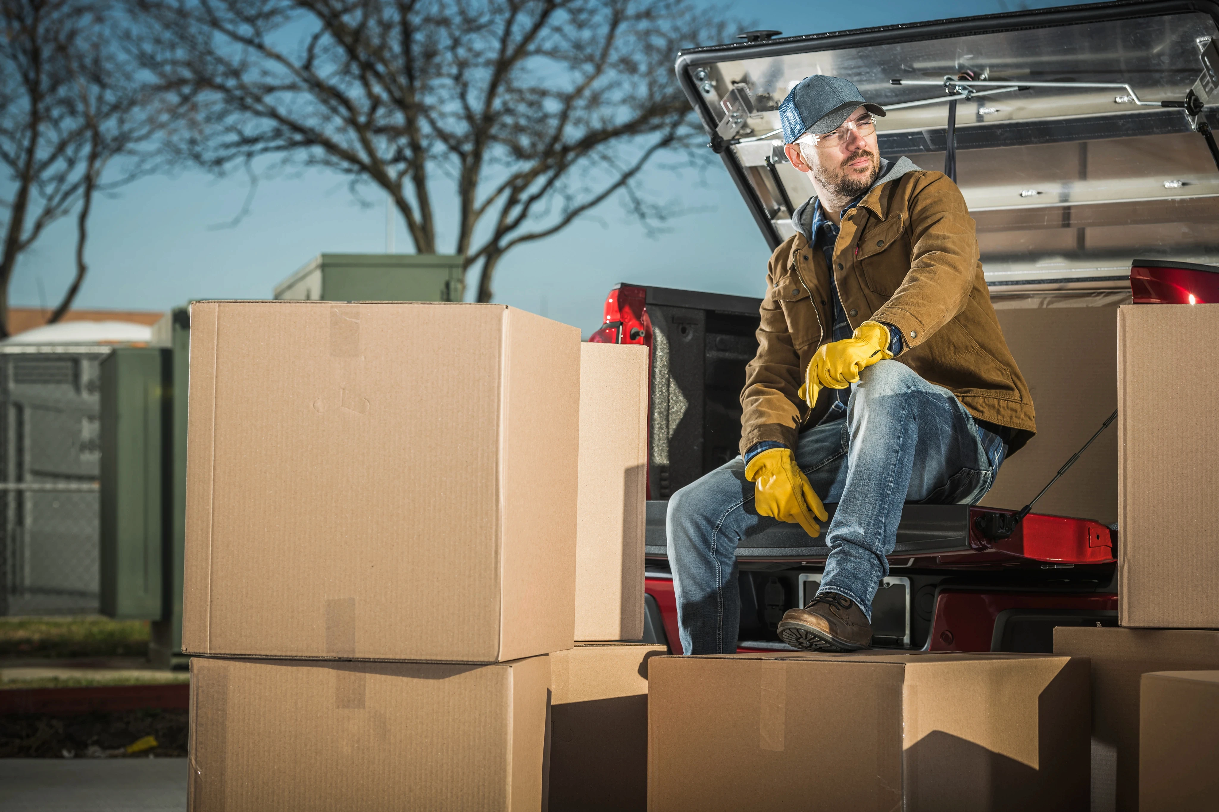 Professional mover sitting on cardboard boxes next to an open moving truck.