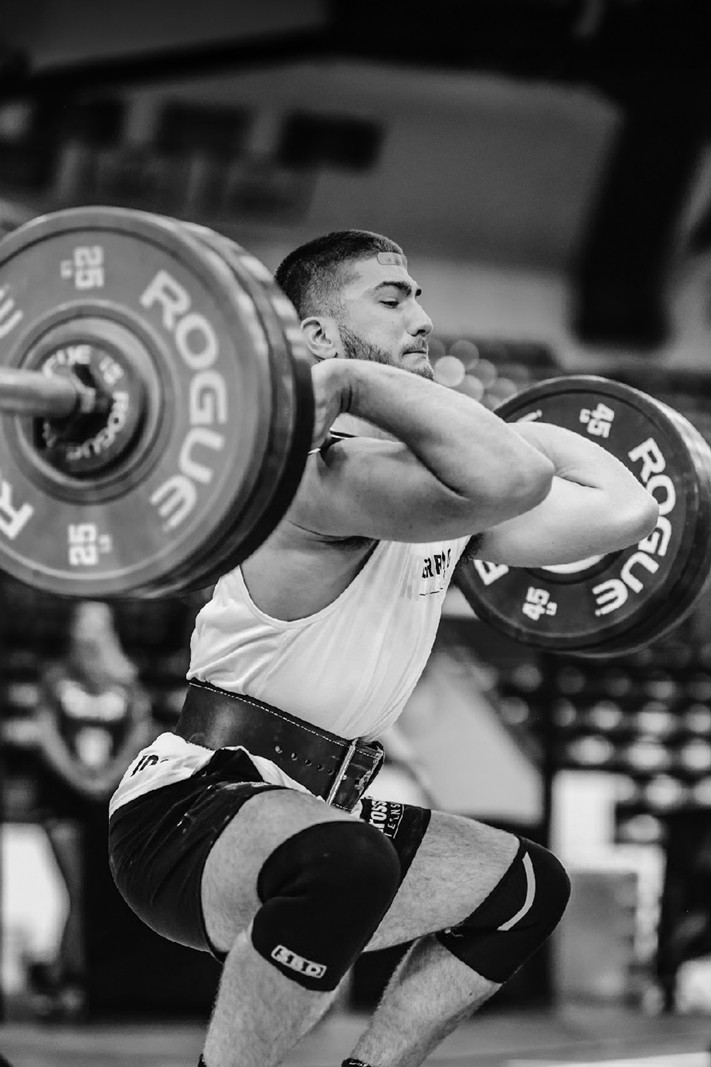 A man with defined abs holding onto a vertical pole in a gym, looking to the side.
