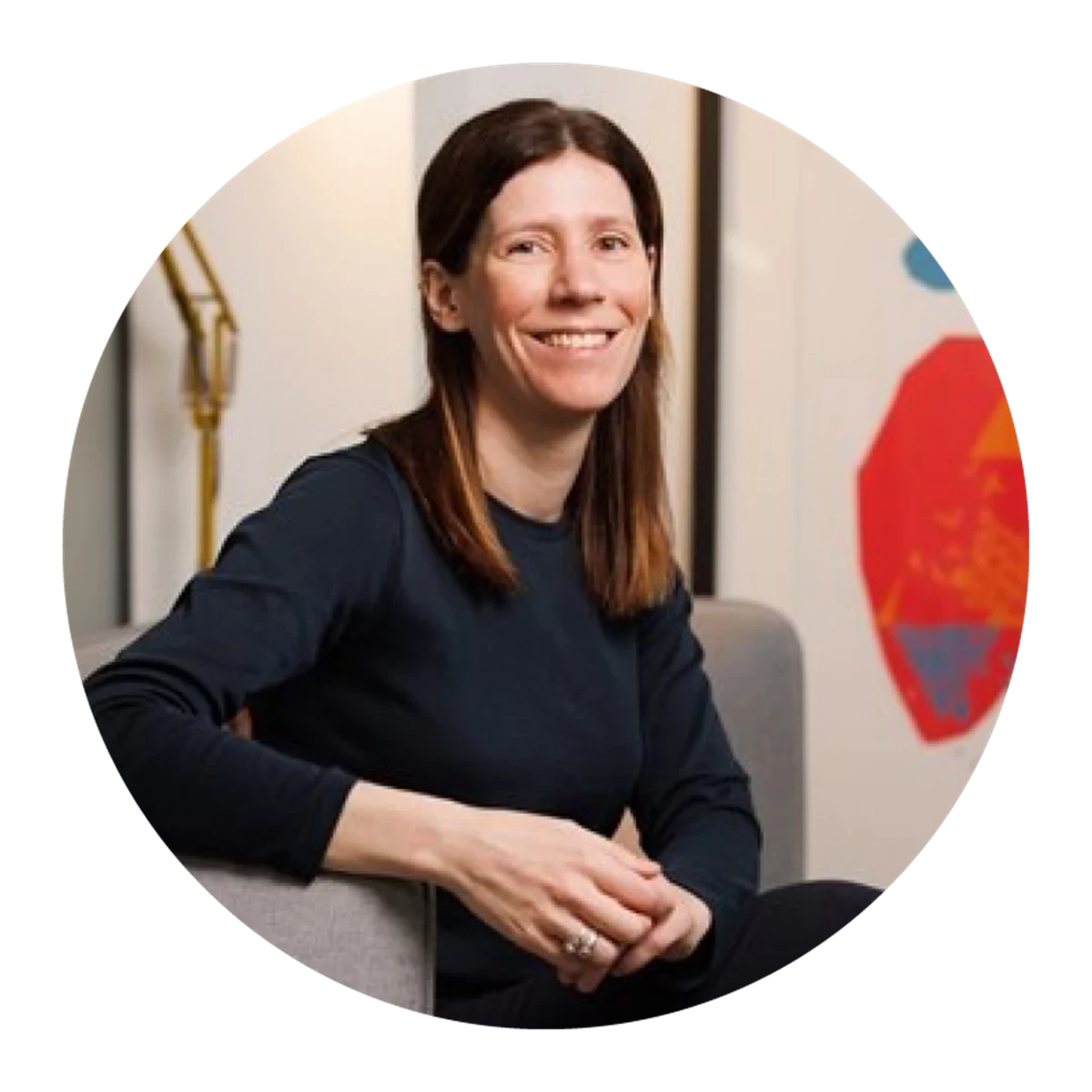 A person sits on a sofa wearing a dark long‑sleeved top. A colourful abstract artwork hangs on the wall behind them.