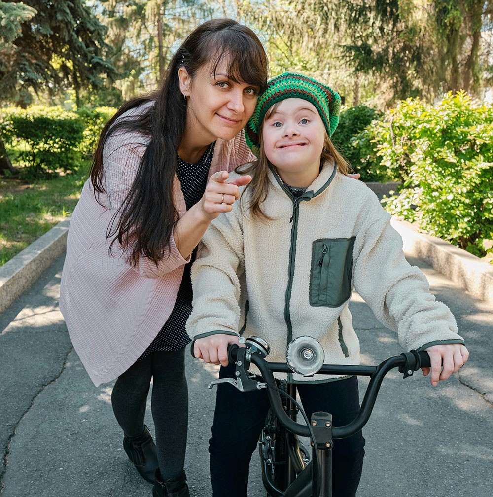 Woman and child on a bike path. The woman is leaning toward the child who is sitting on a bike.