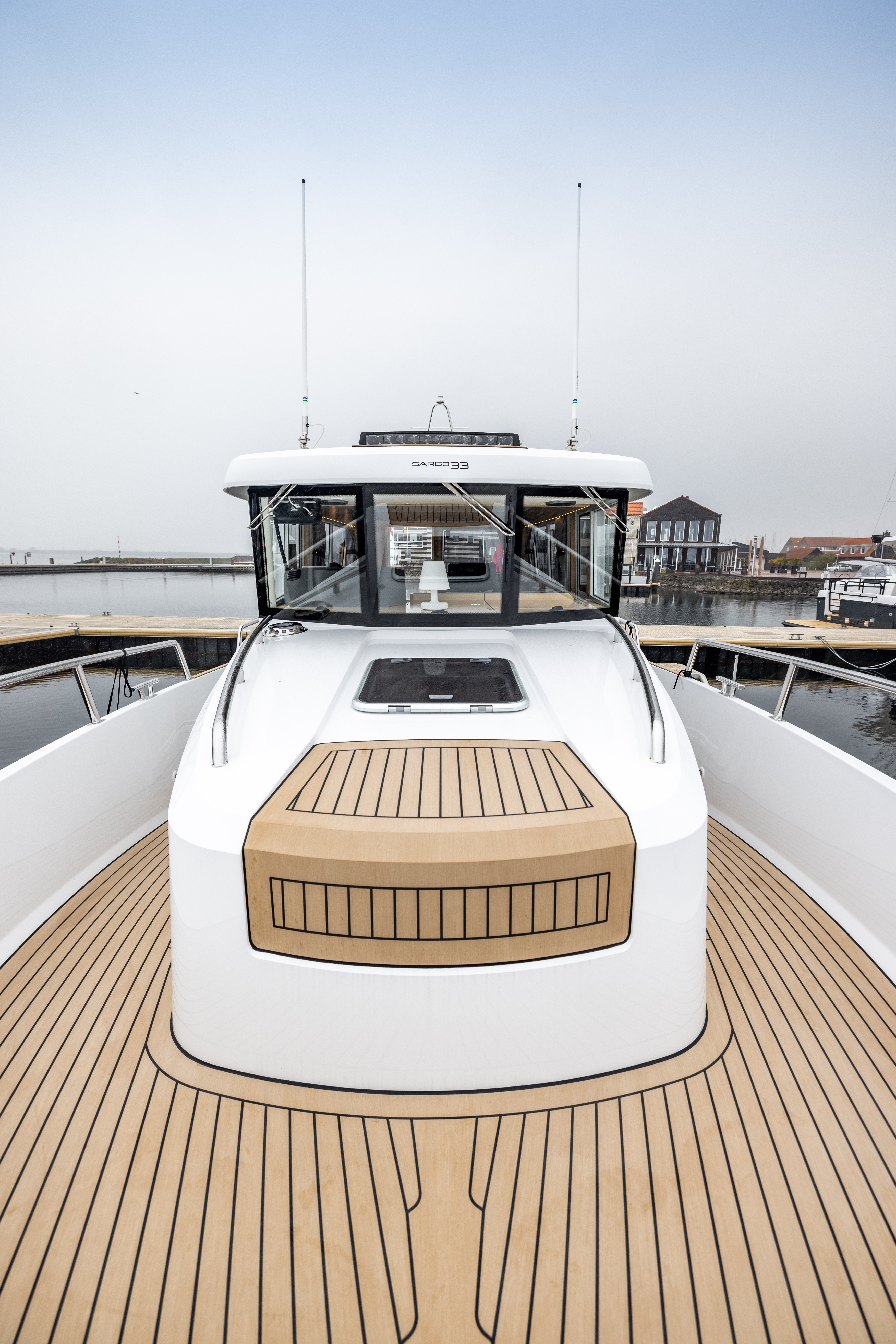 Eye-level perspective from the swim platform looking forward across a wide open motor yacht cockpit, showing EcoDeck light oak composite decking covering the full aft cockpit floor with precise plank alignment, black seam detail, and clean curved edges against white fibreglass coamings