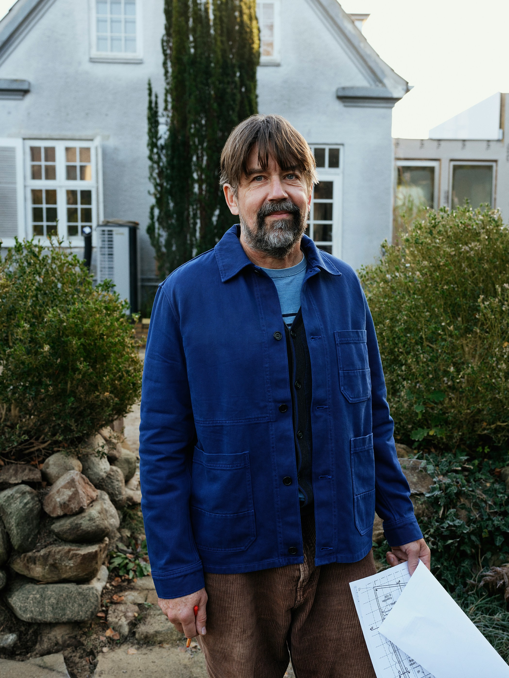 Man in blue jacket standing outside a house.