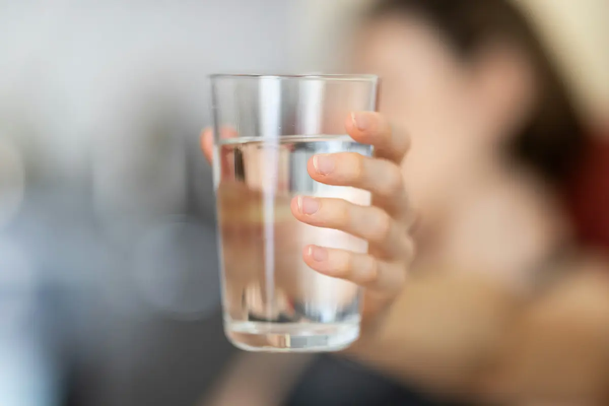 A hand holding a glass of water in the morning light, representing a simple habit that supports energy and recovery.