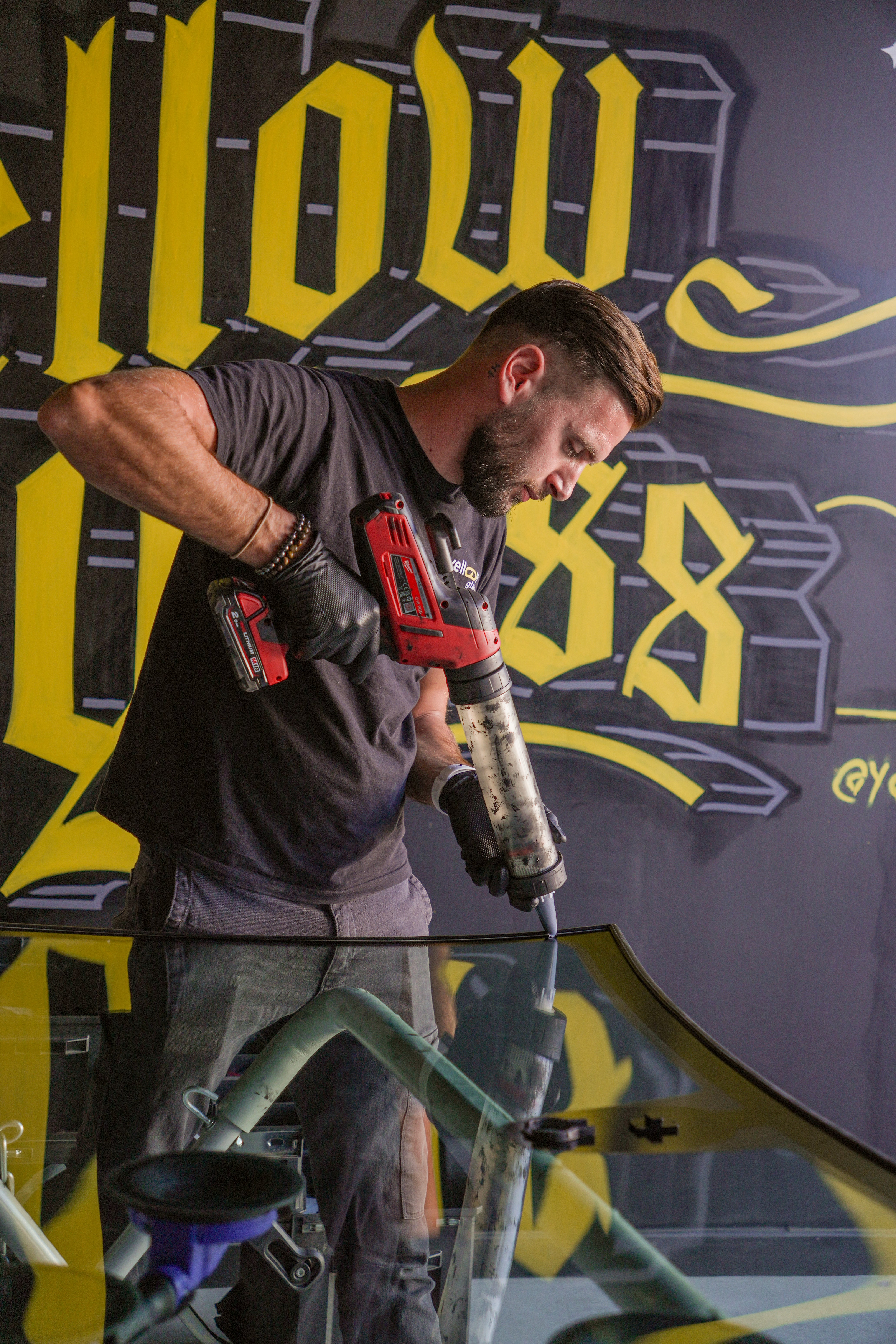 Un homme répare le pare-brise d'une voiture, atelier de réparation de vitres automobiles Yellow Glas.
