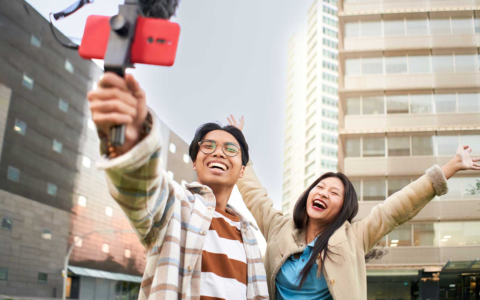 Couple smiling and taking a selfie in Singapore city with modern buildings in the background.