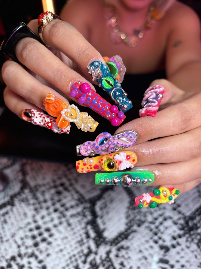  Extreme square-shaped nails featuring a chaotic, vibrant mix of 3D charms: a green reptile eye, a purple octopus tentacle, orange swirls, pearls, and metallic silver beads.
