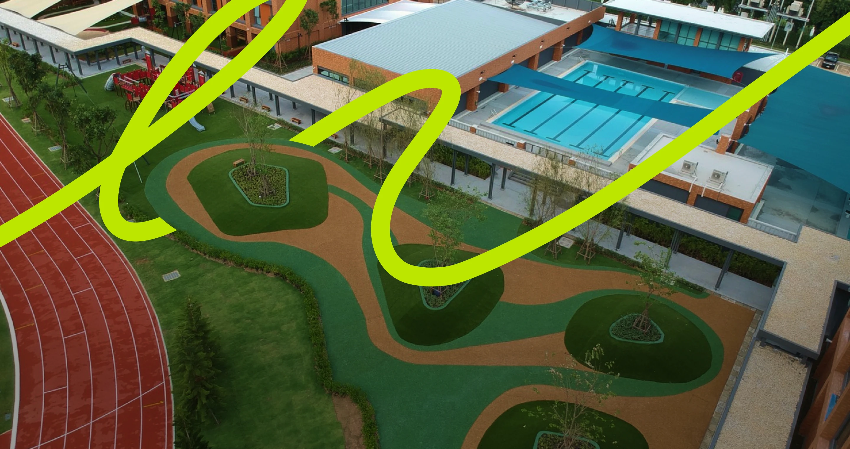 Aerial view of a modern sports complex featuring a red running track, abstract green and tan landscaping, and adjacent blue swimming pools.