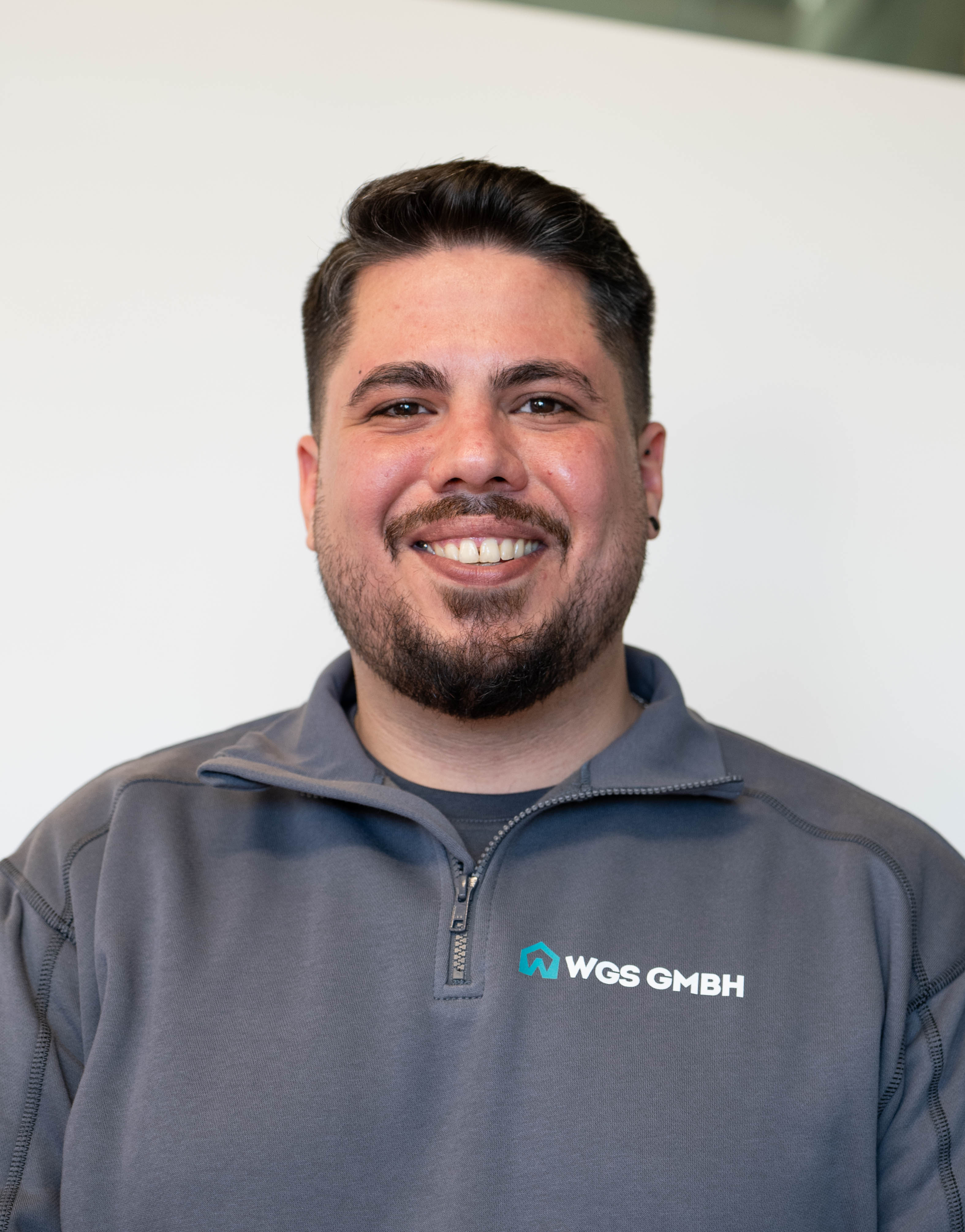 A woman with short curly hair wearing a black t-shirt looks into the camera.