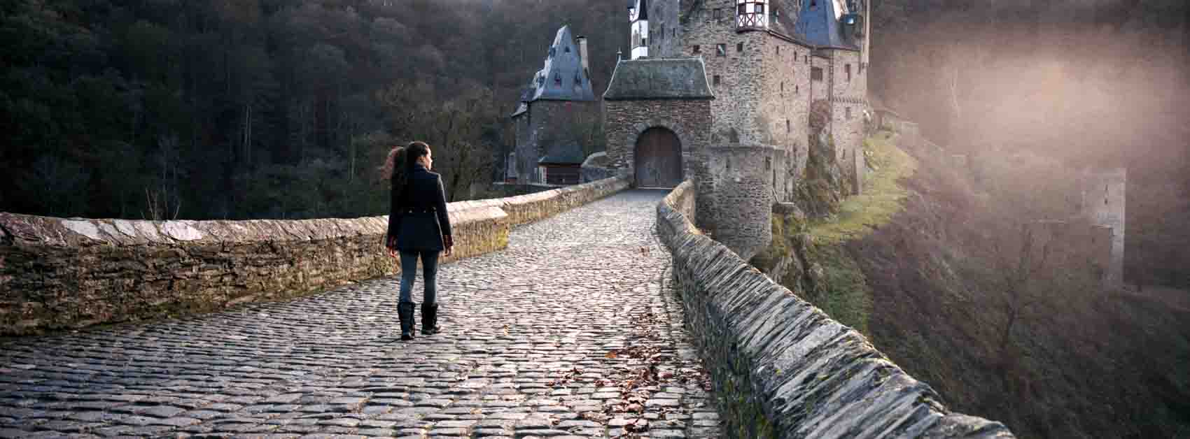 A film photograph of a person on a bridge walking towards a castle with a lens flare