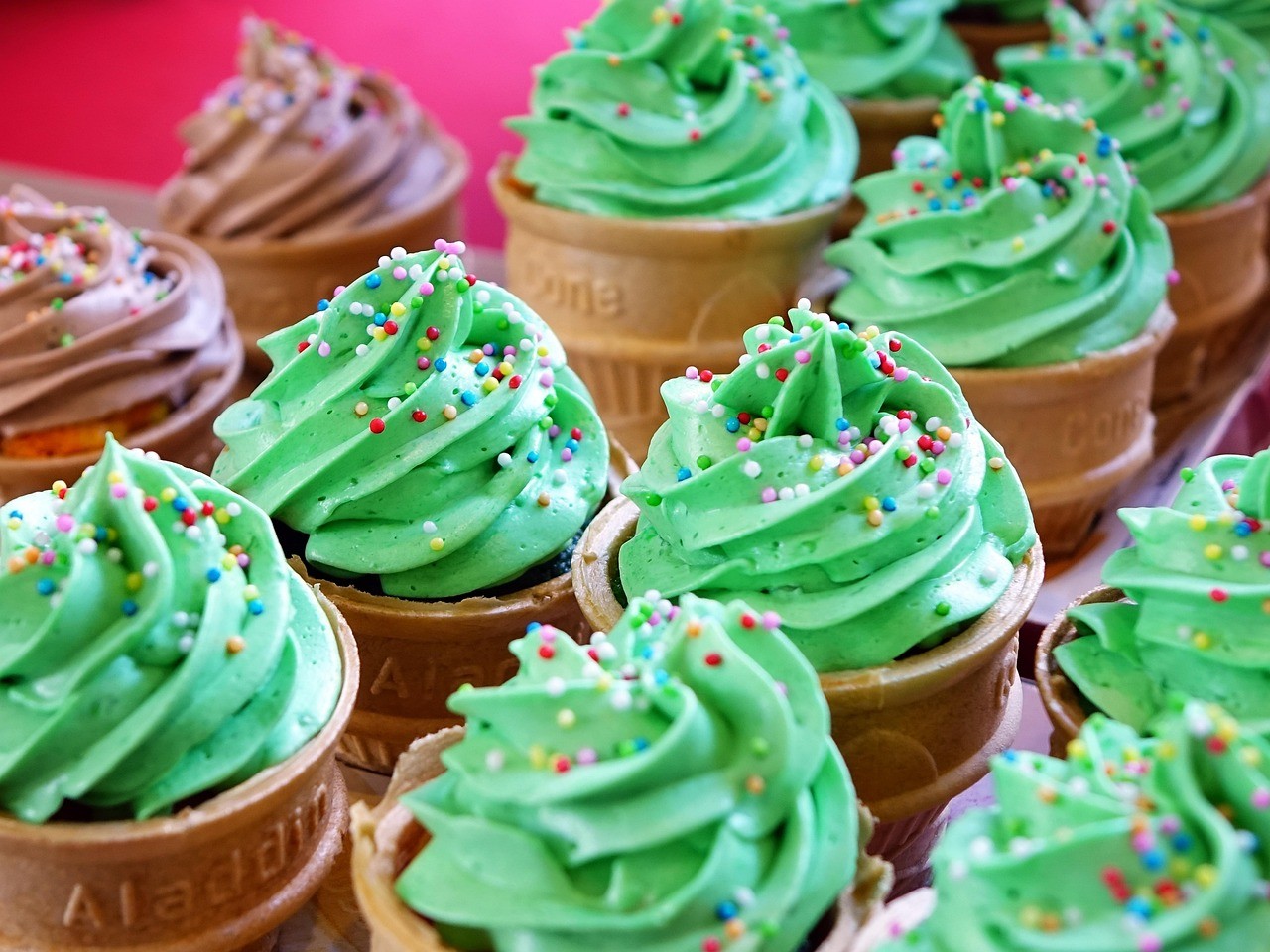 A close-up of several dessert cups filled with green swirled frosting, arranged attractively on a colorful surface.
