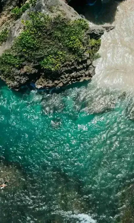 Aerial view of a stunning Bali beach and surfers, showcasing the tropical lifestyle of our multi-style yoga teacher training retreat