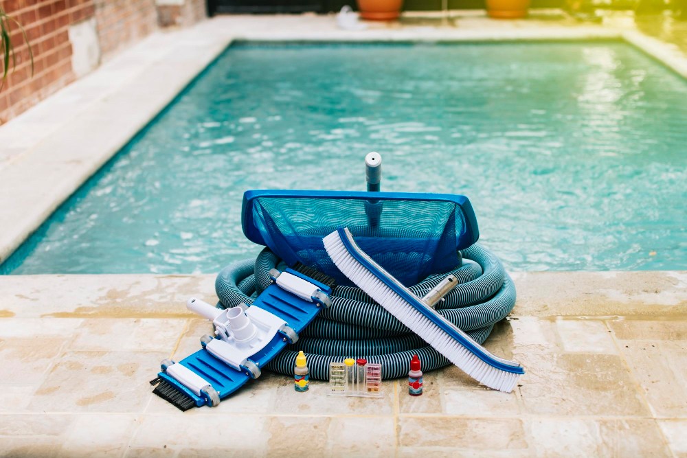 Pool cleaning equipment, hoses, test kits and a leaf net laid out beside a residential swimming pool.