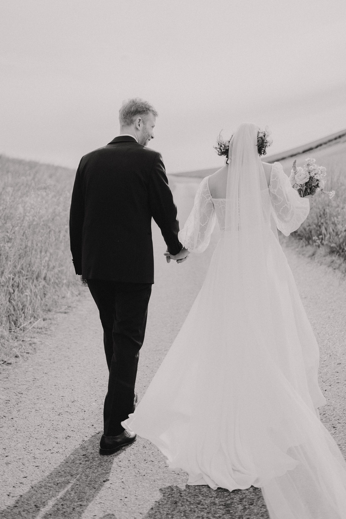 Zeitloses Schwarz-Weiß-Foto eines Brautpaares von hinten auf einem Feldweg