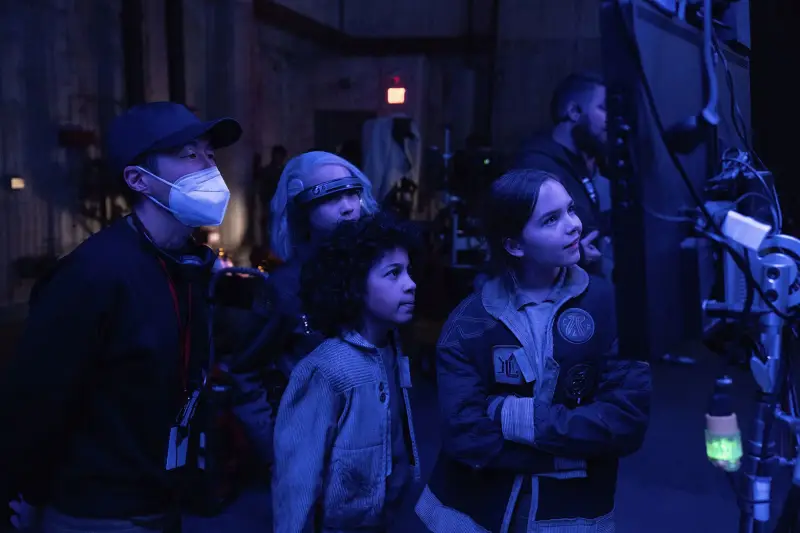 A group of four crew members discuss with an actor in costume on a movie set, surrounded by textured backdrop.