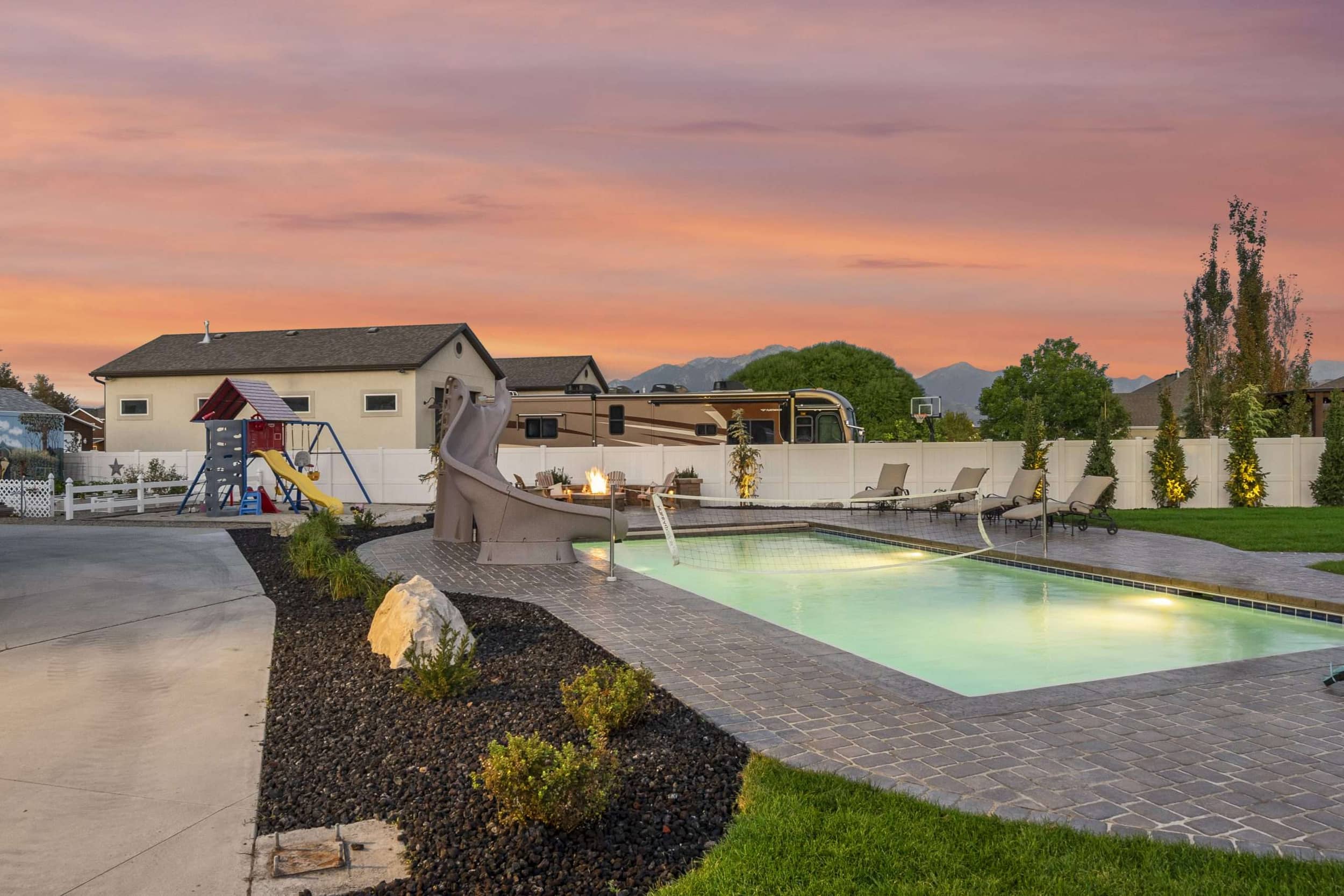 Riverton Residence circular natural-stone fire pit and paver seating beside the pool at dusk