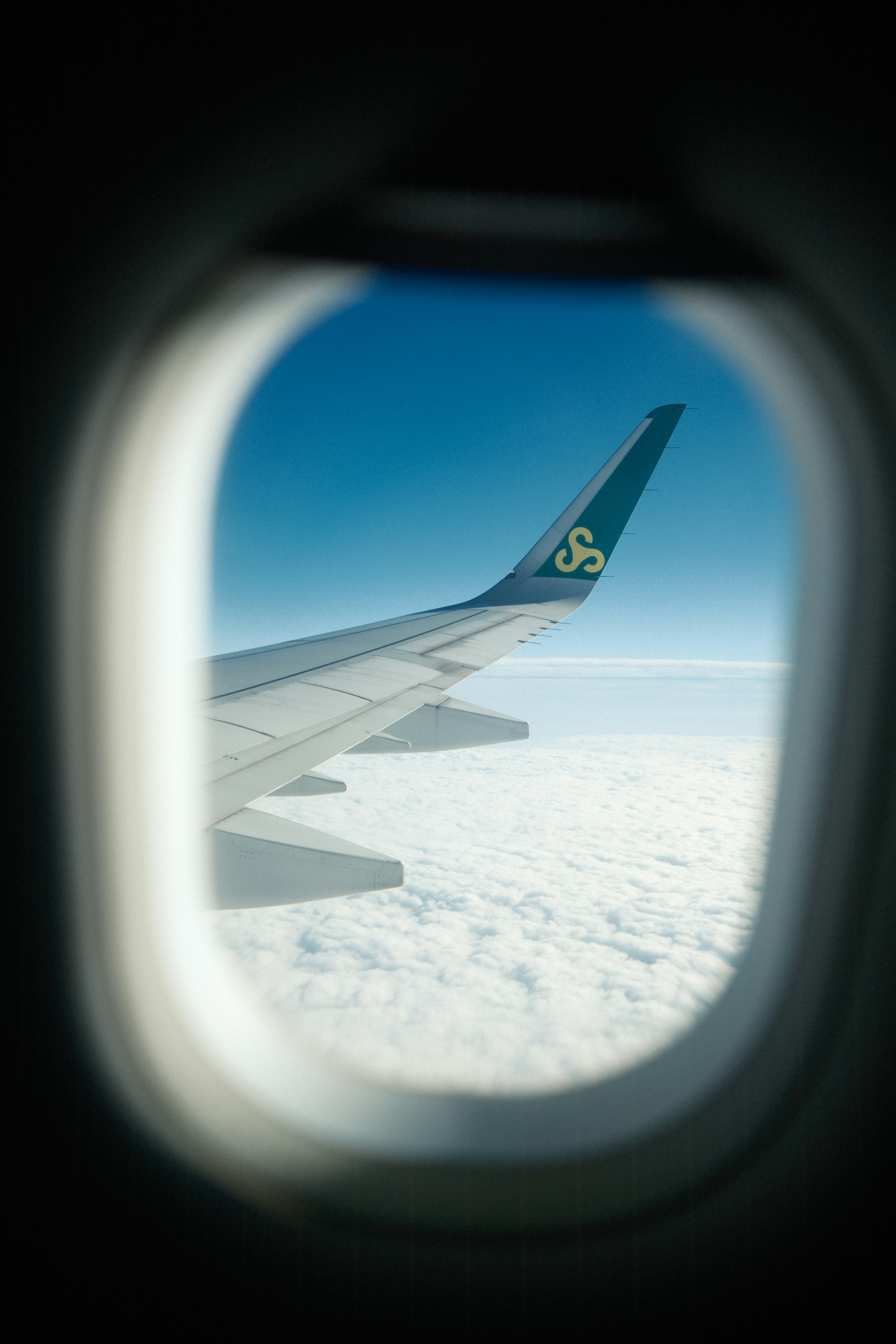 A young person with curly hair smiles at the camera while sitting in front of a laptop against a dark background.