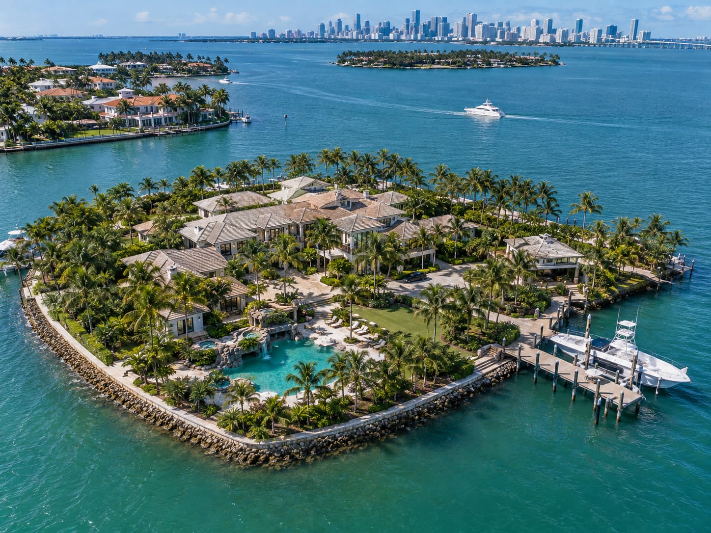 Aerial daytime view of a sprawling luxury waterfront compound, showing the resort-style pool, private dock with boat davits, landscaped grounds, motor court, and surrounding island waterways beneath clear blue skies.