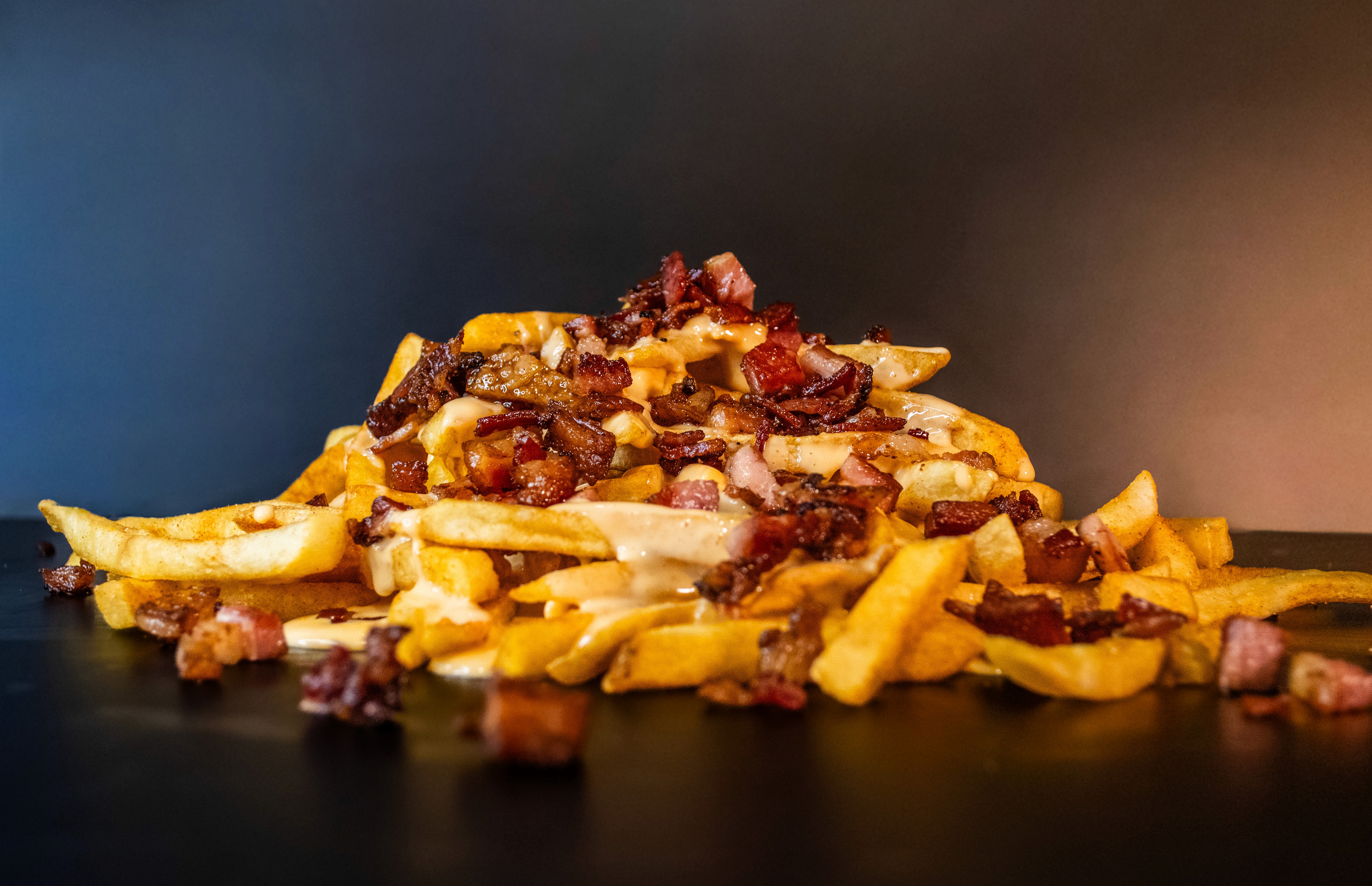 Porción de papas con salsa cheddar y bacon bits.